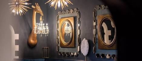 A room with a dark wall, a chandelier, a large mirror, and a decorative giraffe head.