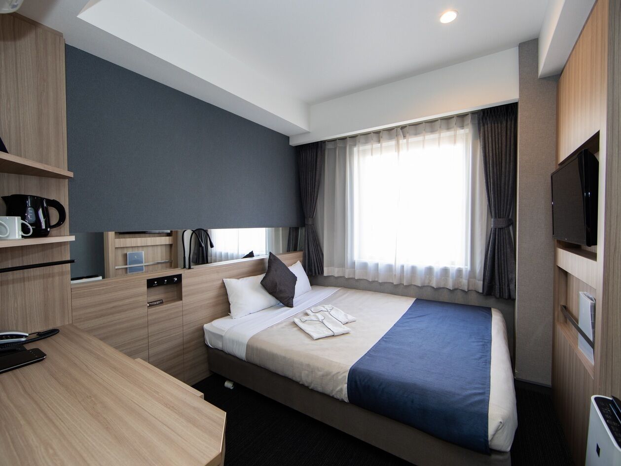 A hotel room with a bed, a desk, a television, and a window with curtains.