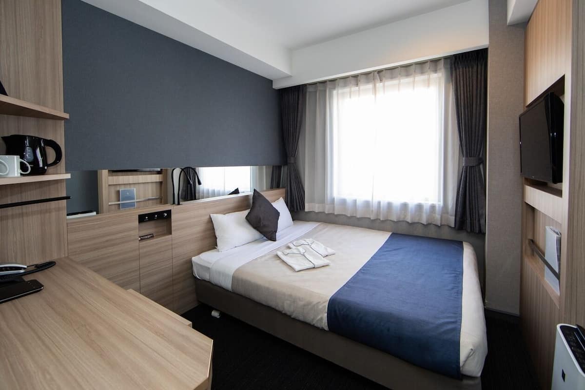 A hotel room with a bed, a desk, a television, and a window with curtains.
