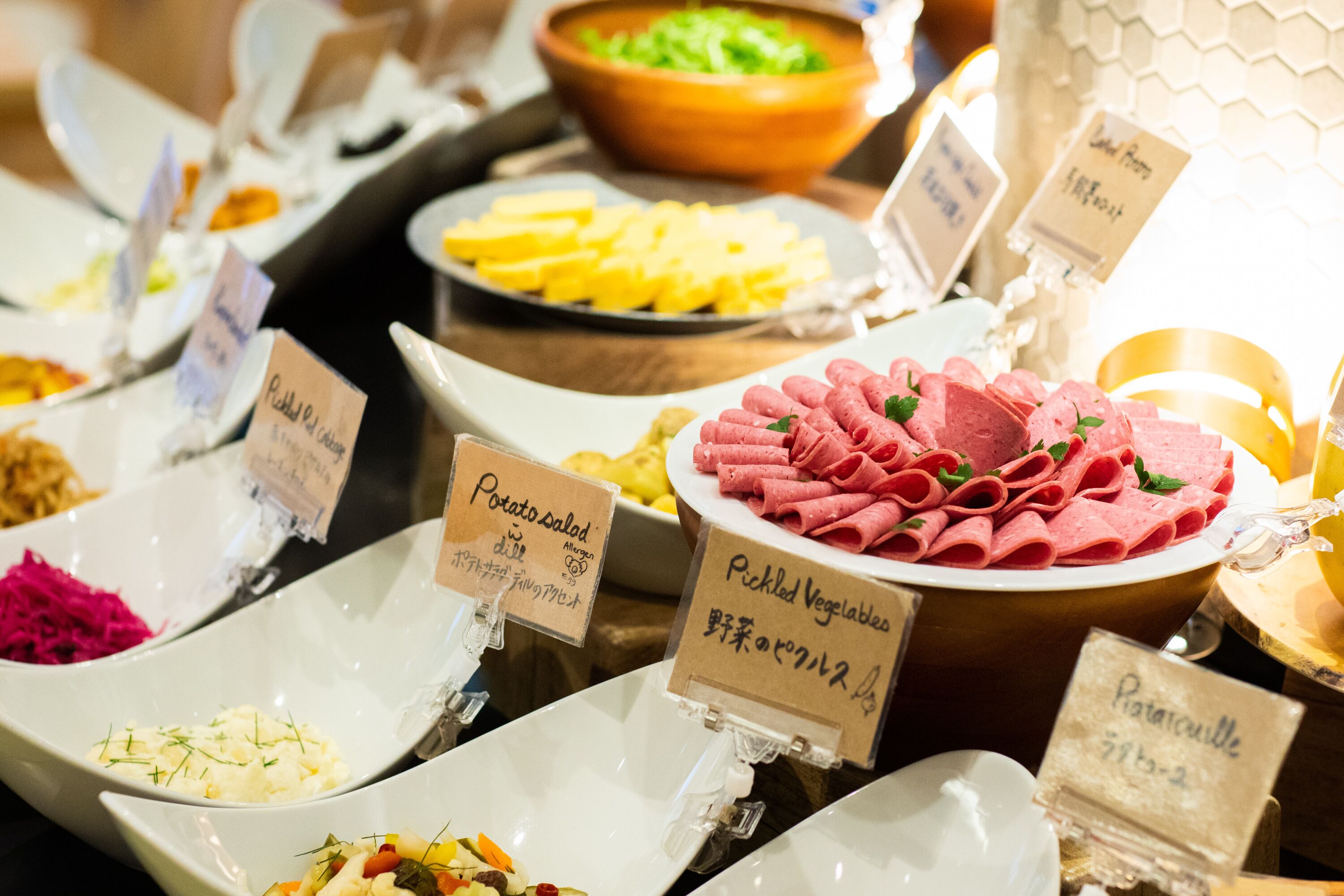 A buffet with labeled dishes including potato salad, pickled vegetables, and a variety of other items.