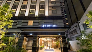 Das Äußere eines Hotels im modernen Design, mit einem markanten Eingangsbereich, Glasüren und einem Schild mit der Aufschrift 'QUINTESSA'.