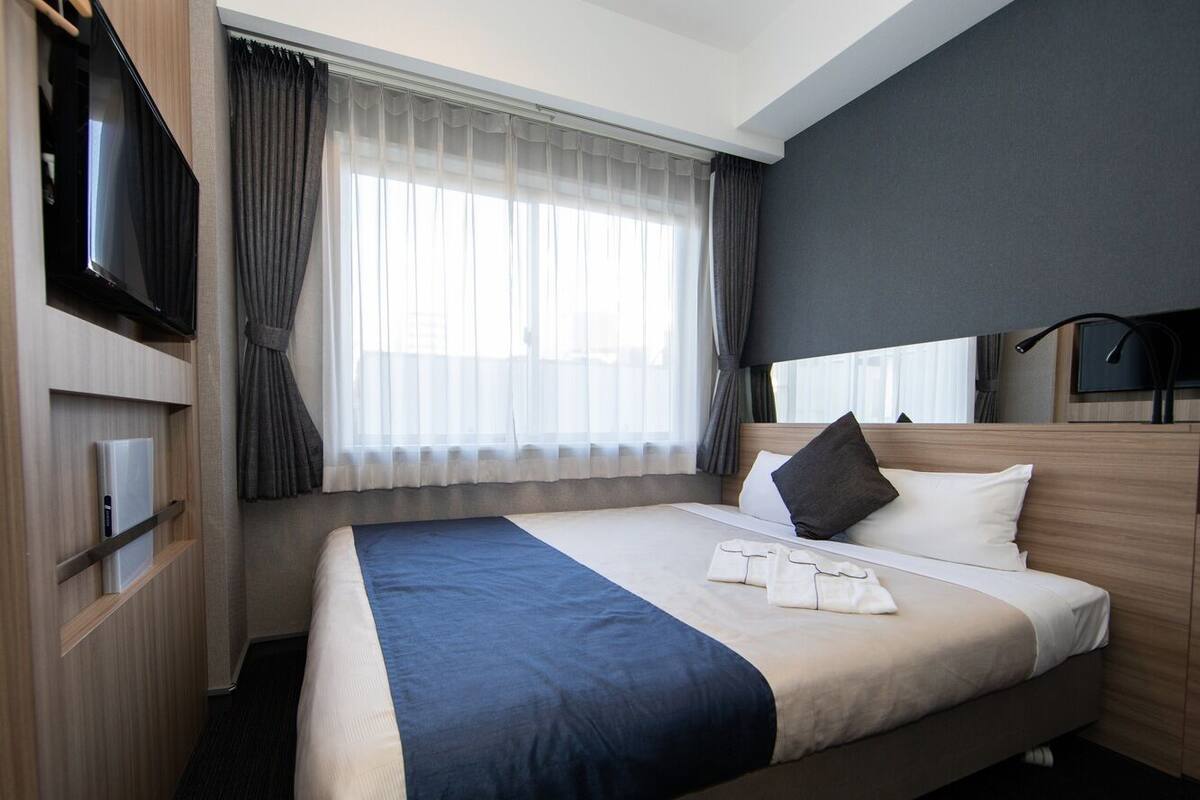 A hotel room with a bed, a TV, a desk with a computer, and a window with curtains.