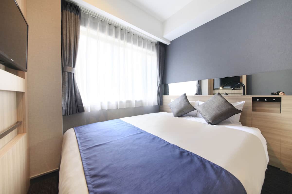 A hotel room with a large bed, a flat-screen TV, a desk, and a window with curtains.