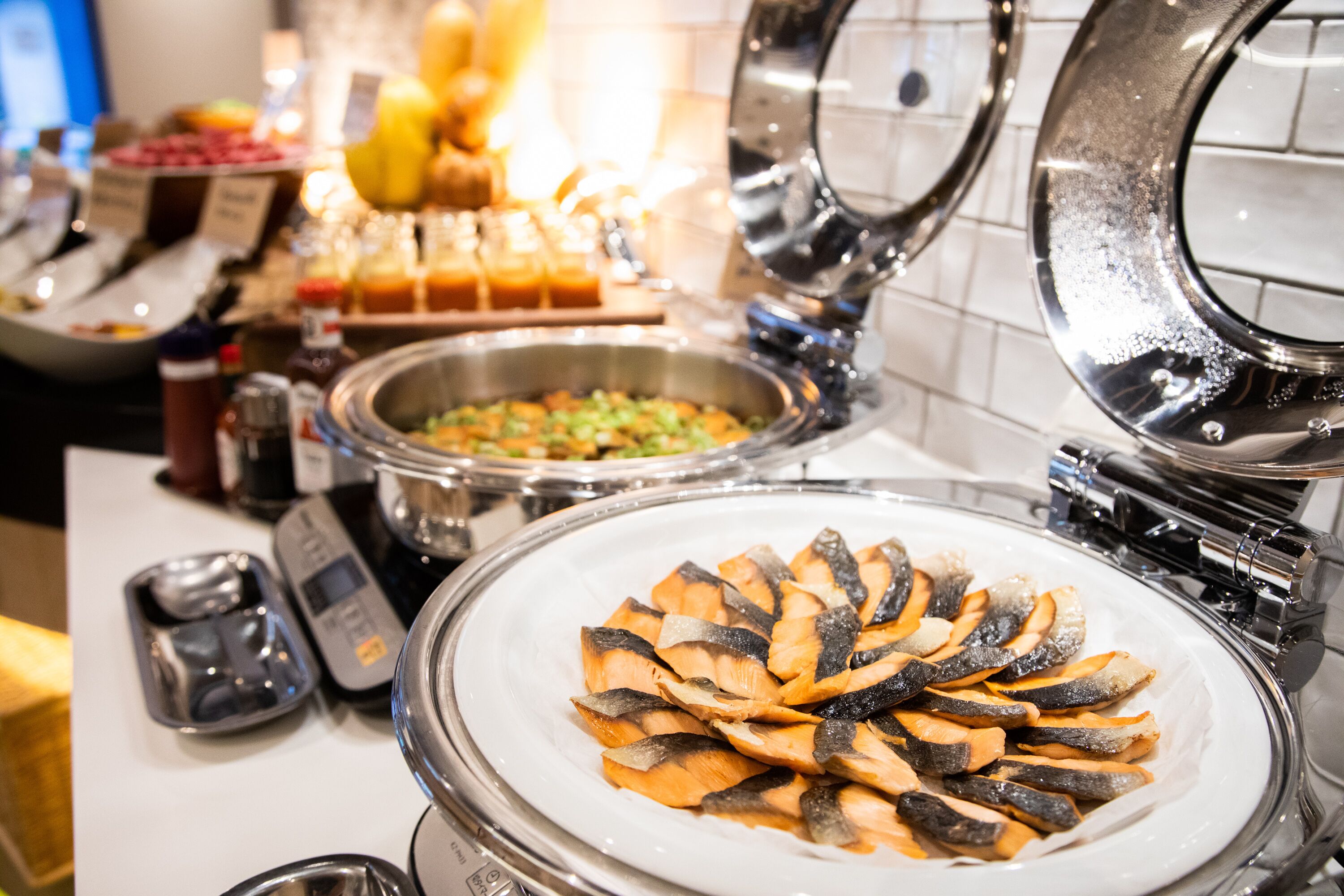 A buffet with various food items including a plate of sliced fish, a bowl of mixed vegetables, and a container of sauces.