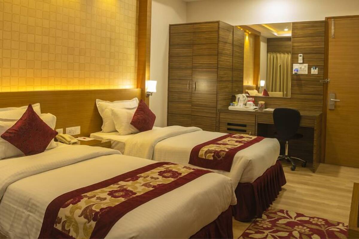 A hotel room with two beds, a desk, a chair, and a wardrobe.