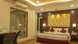 A hotel room with a bed, bedside table, lamp, and a desk with a chair. - Hotel Harrison Palace (Biratnagar)