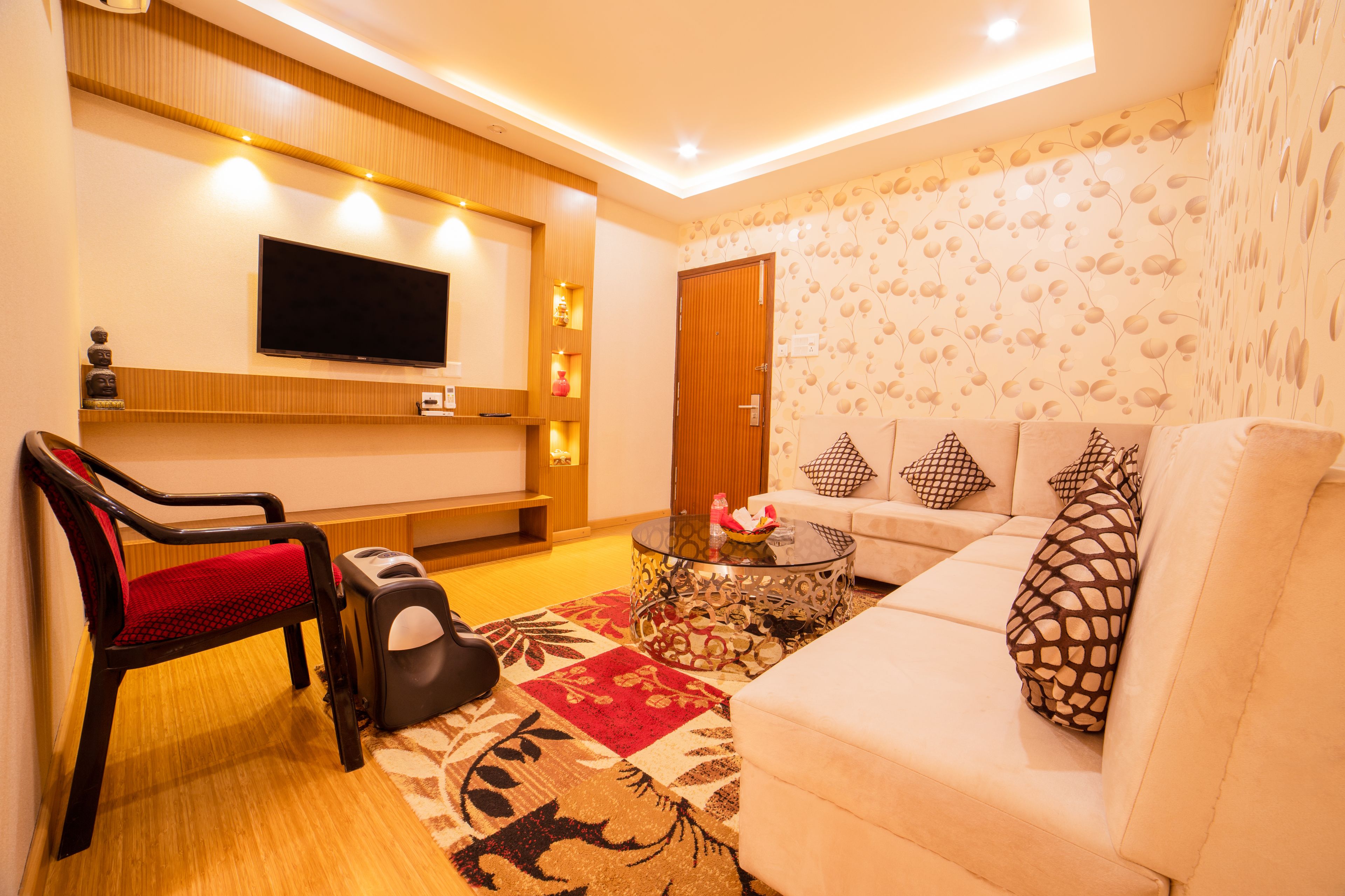 A modern living room with a sofa, a red chair, a glass coffee table, and a flat-screen TV mounted on the wall.
