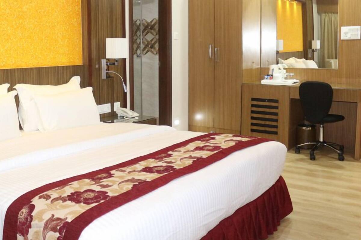 A hotel room with a large bed, a desk with a chair, a wardrobe, and a mirror.