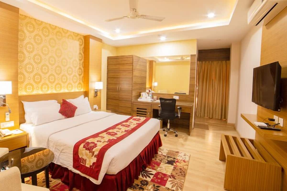A hotel room with a bed, a desk, a chair, a TV, and a ceiling fan.