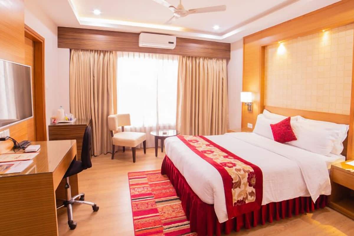 A hotel room with a bed, desk, chair, TV, and a desk lamp.