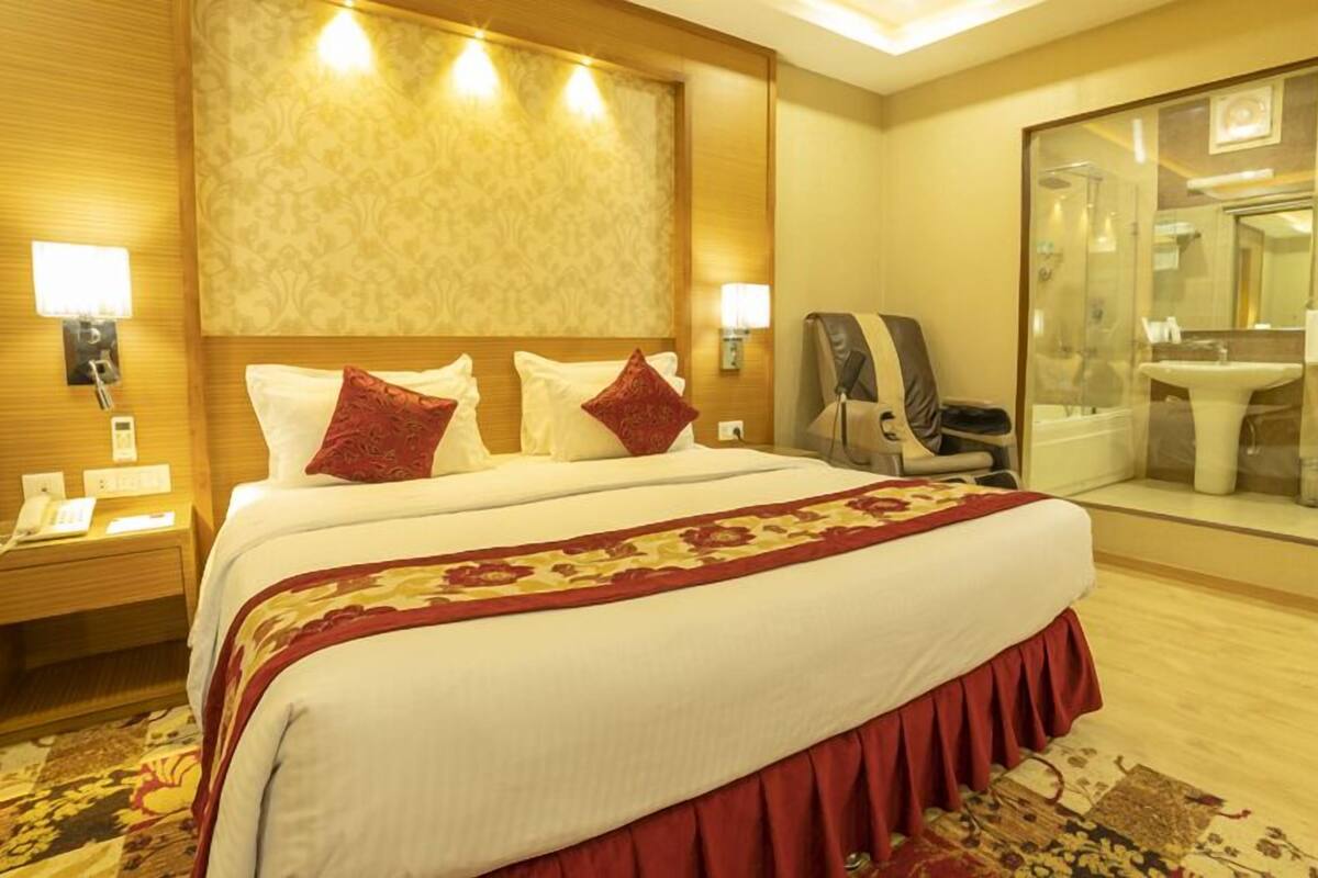 A hotel room with a large bed, a nightstand with a phone, a chair, and a bathroom with a sink and mirror.