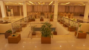 A spacious lobby with a central staircase, multiple seating areas, and potted plants. - Hotel Harrison Palace (Biratnagar)
