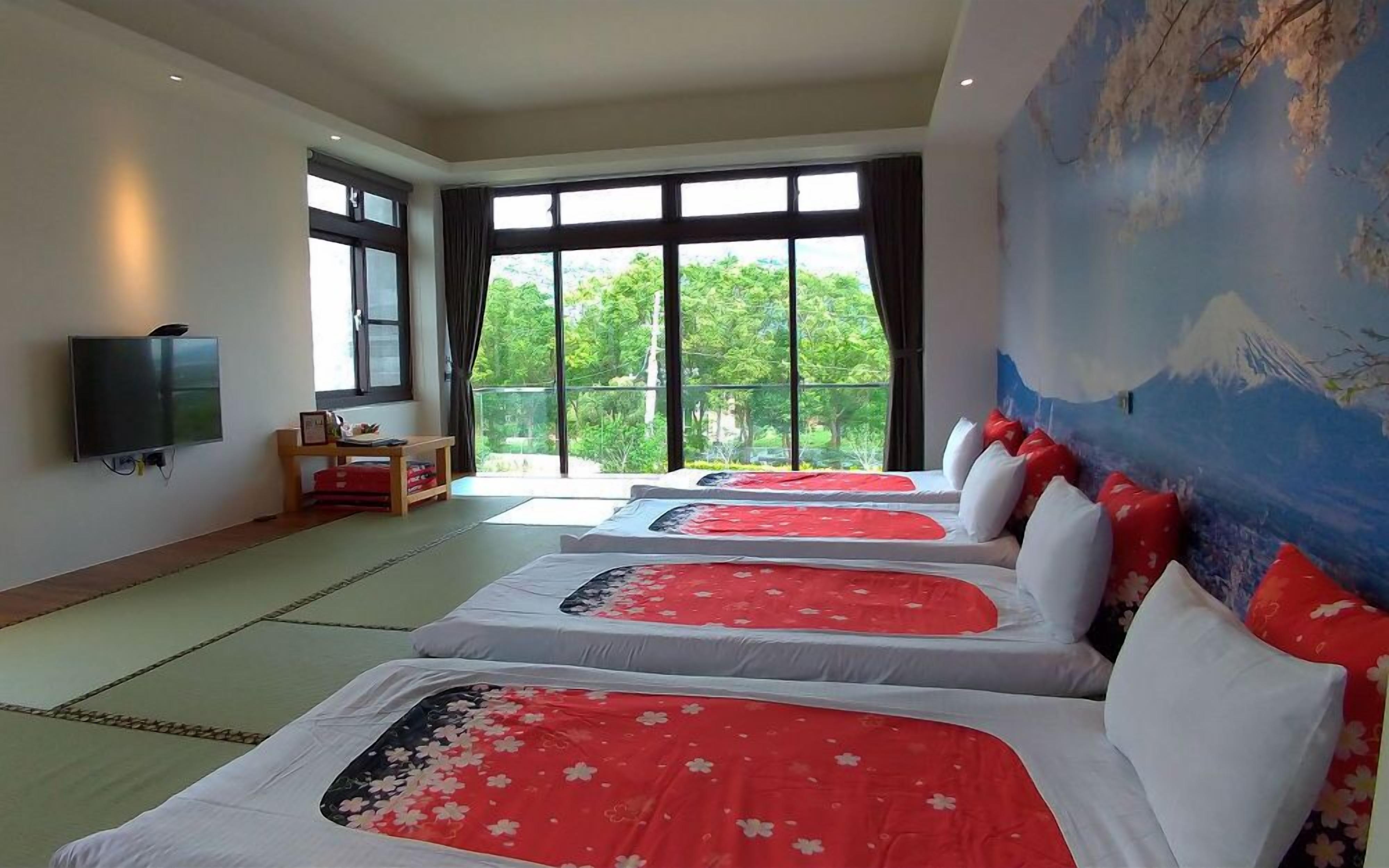 A hotel room with two beds, a TV, and a balcony with a view of trees.