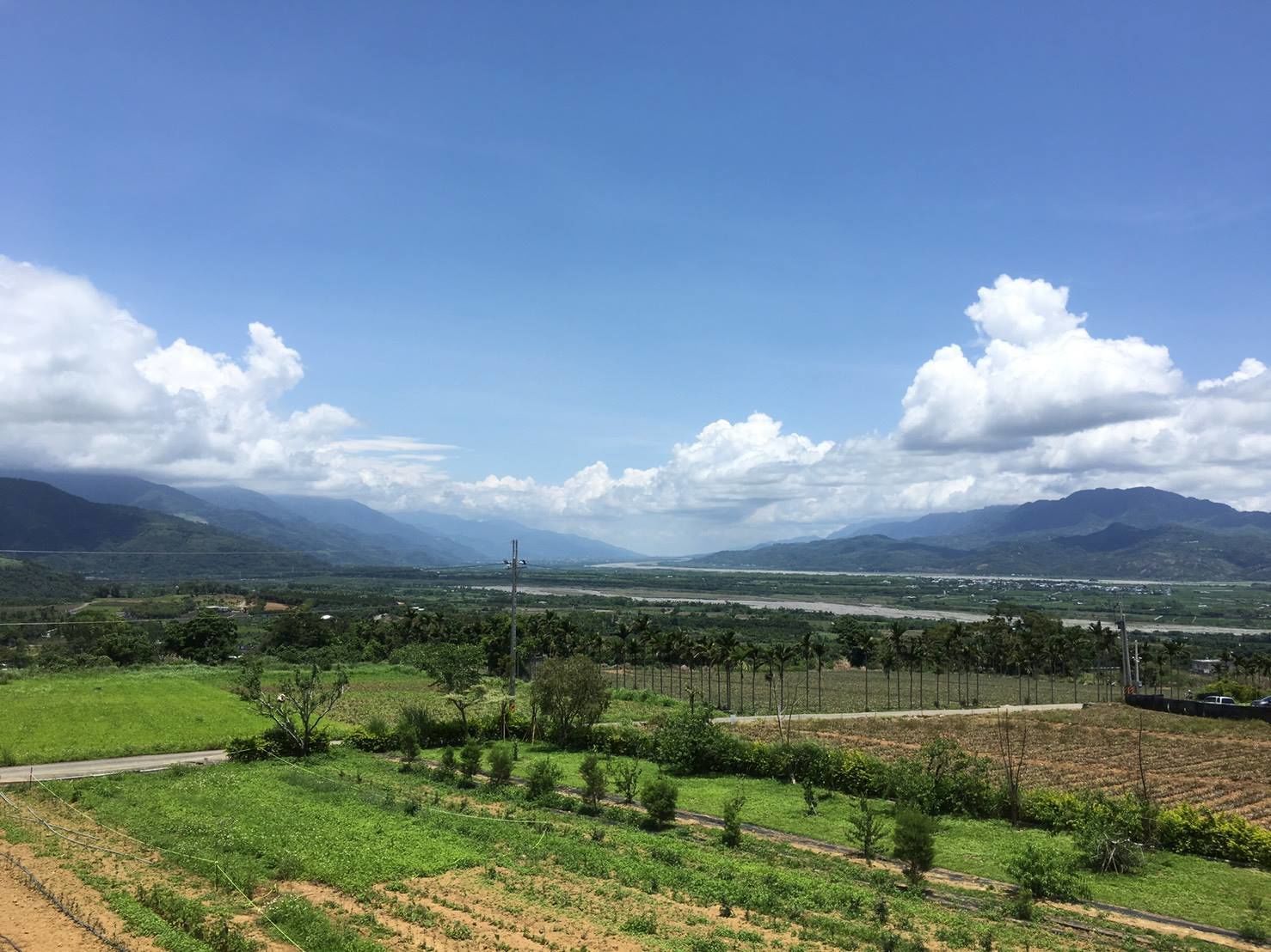 A rural landscape with fields, a road, and distant mountains under a clear sky.