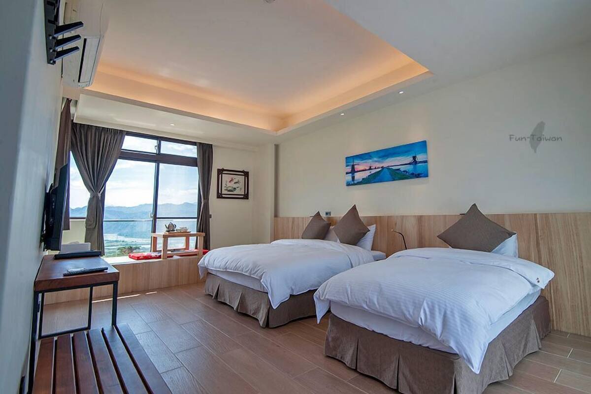 A hotel room with two beds, a desk, and a window with a view of the mountains.