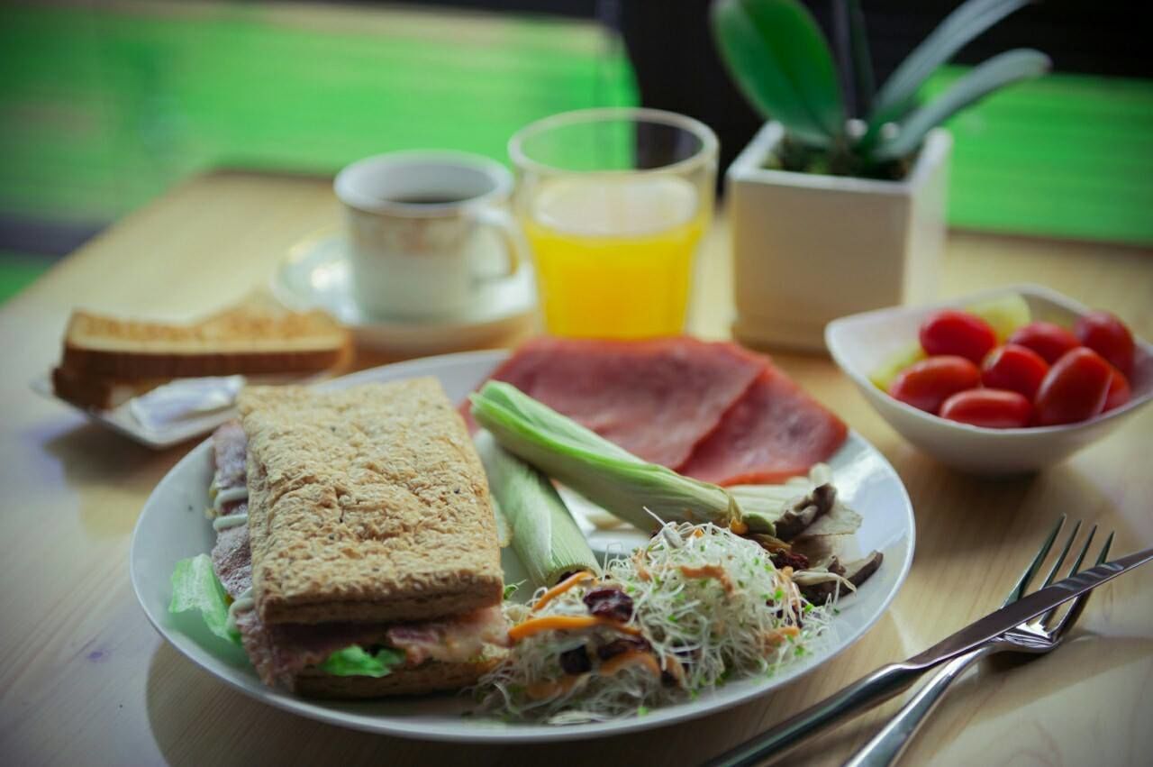 Prato de café da manhã com sanduíche, legumes e um copo de suco de laranja.