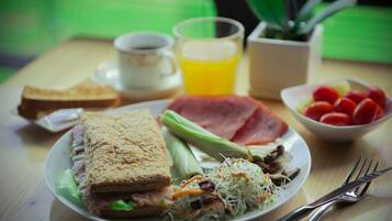 Prato de café da manhã com sanduíche, legumes e um copo de suco de laranja.