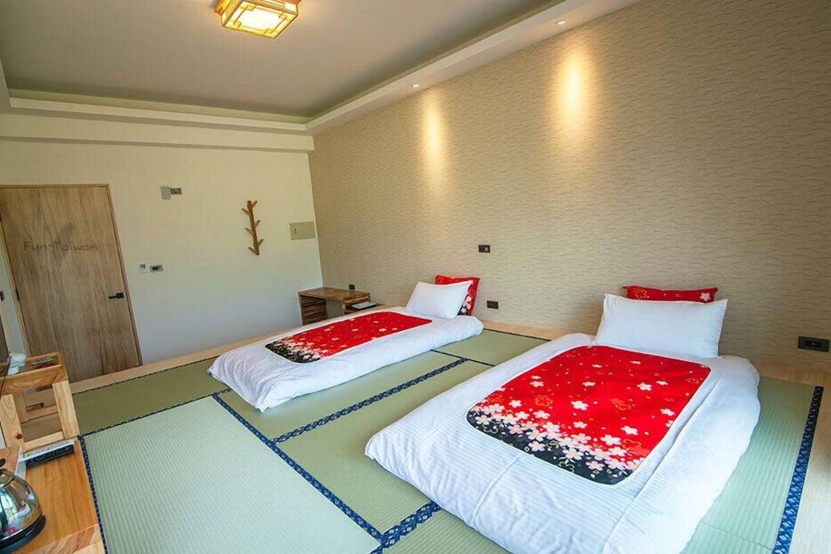 A hotel room with two beds, tatami mats, a wooden door, a small table, and a television.