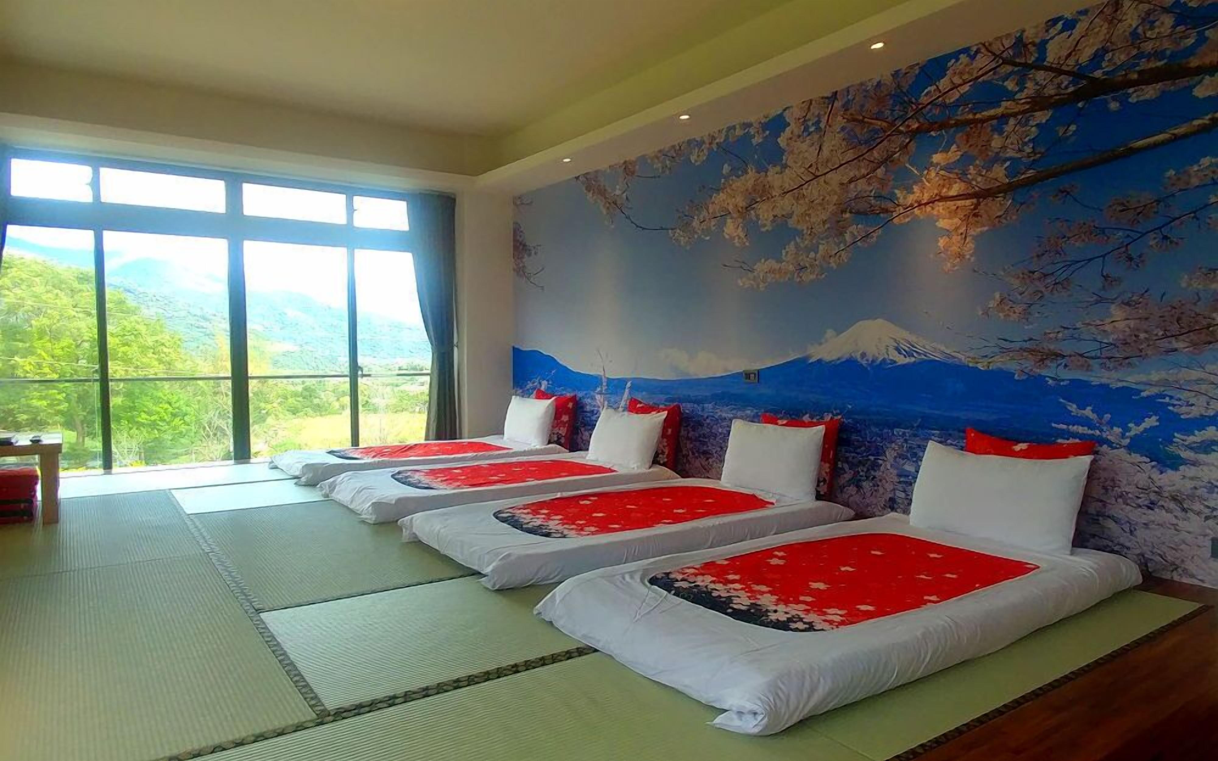 Une chambre avec trois lits alignés le long d’un mur orné d’une fresque représentant le mont Fuji.