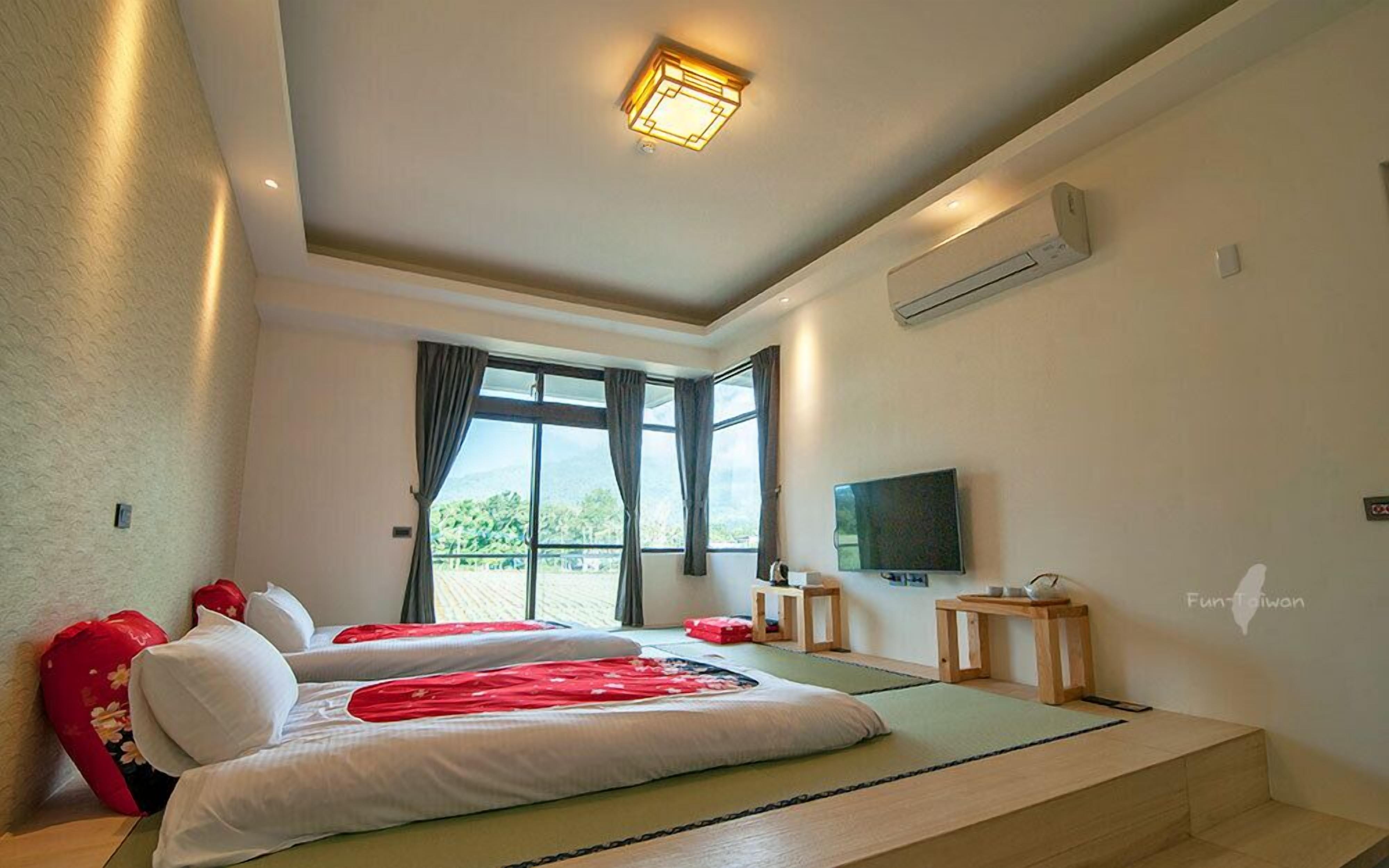 A hotel room with two beds, a TV, and a balcony with a view of greenery.