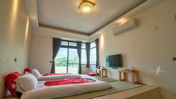 A hotel room with two beds, a TV, and a balcony with a view of greenery.