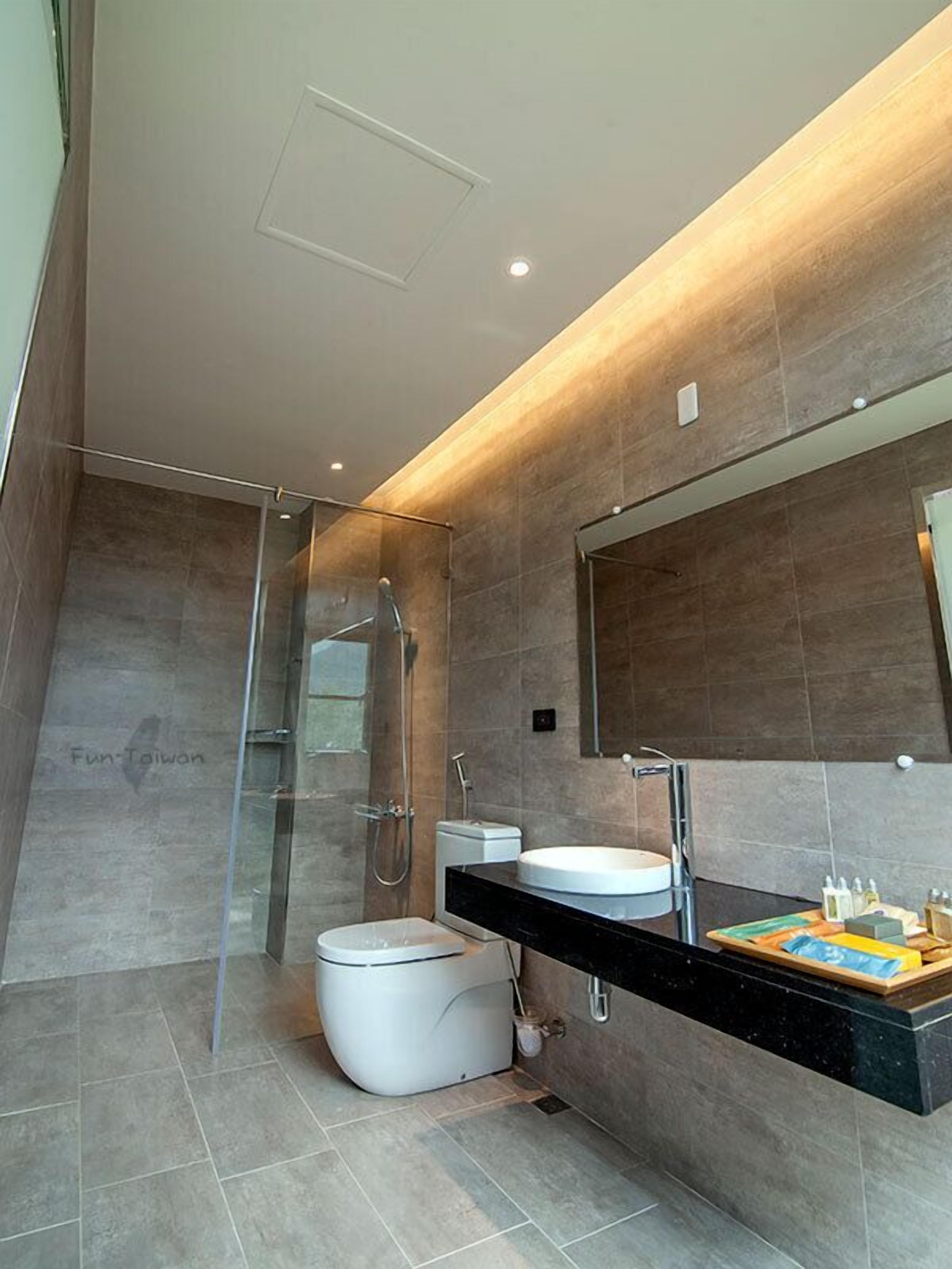 Une salle de bain moderne avec une douche à l’italienne en verre, des toilettes blanches et un meuble-lavabo noir avec un miroir.