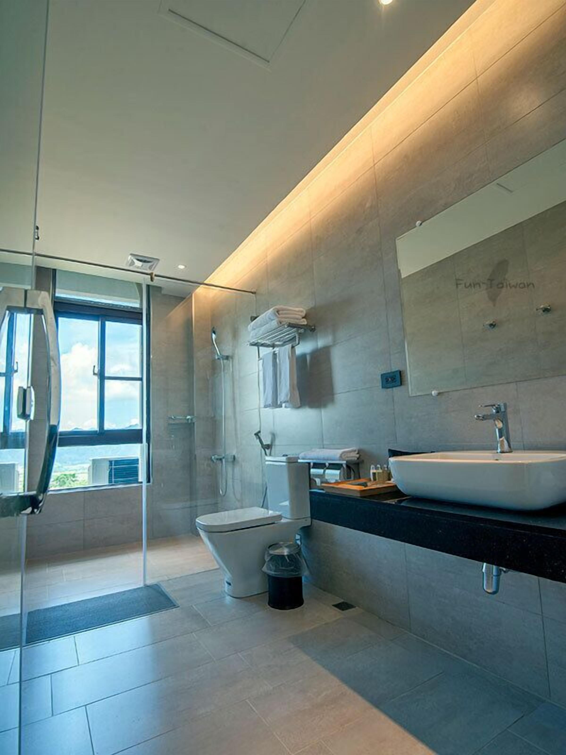 A modern bathroom with a large window, a walk-in shower, a toilet, and a sink.