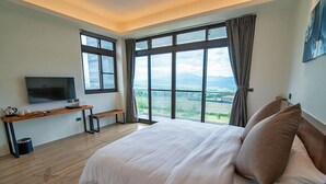 Un dormitorio con una cama grande, un televisor sobre un mueble, un escritorio con un banco y ventanas amplias que ofrecen vistas al campo.
