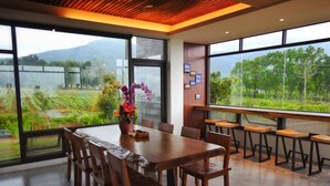 Un comedor moderno con una mesa grande y sillas, ventanas amplias que ofrecen vistas a un paisaje verde, y un techo de madera.