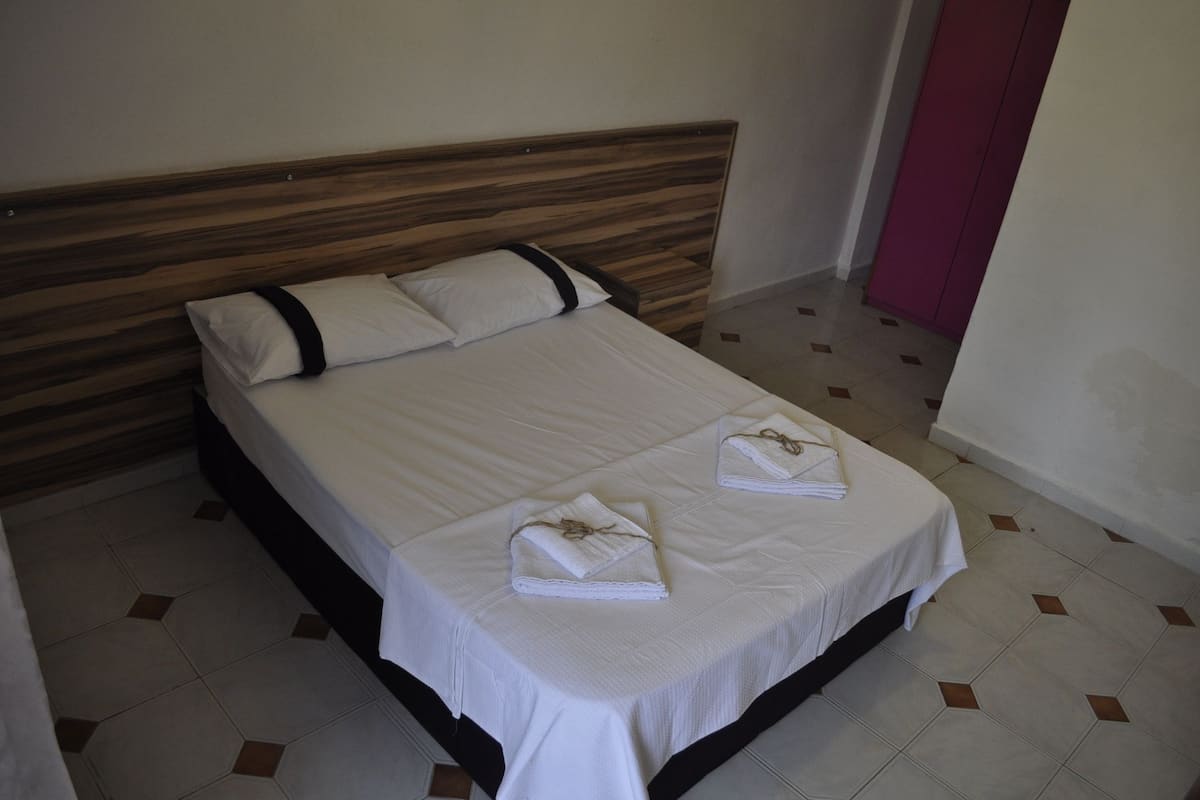 A neatly made bed with a wooden headboard, a pink door, and a tiled floor.