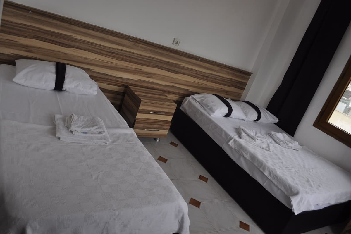 A hotel room with two single beds, a wooden headboard, a small bedside table, and a window with curtains.