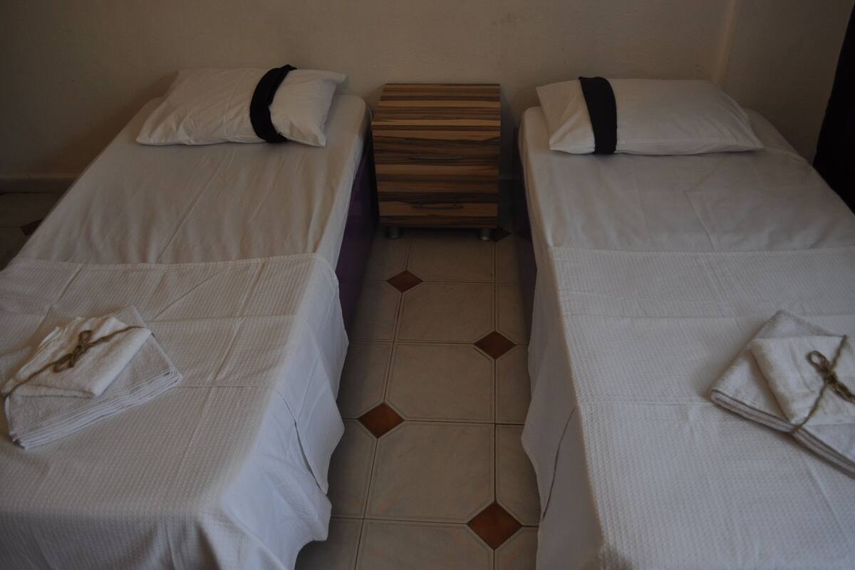 Two single beds with white linens and black headboards, a wooden nightstand between them, and a tiled floor with a diamond pattern.