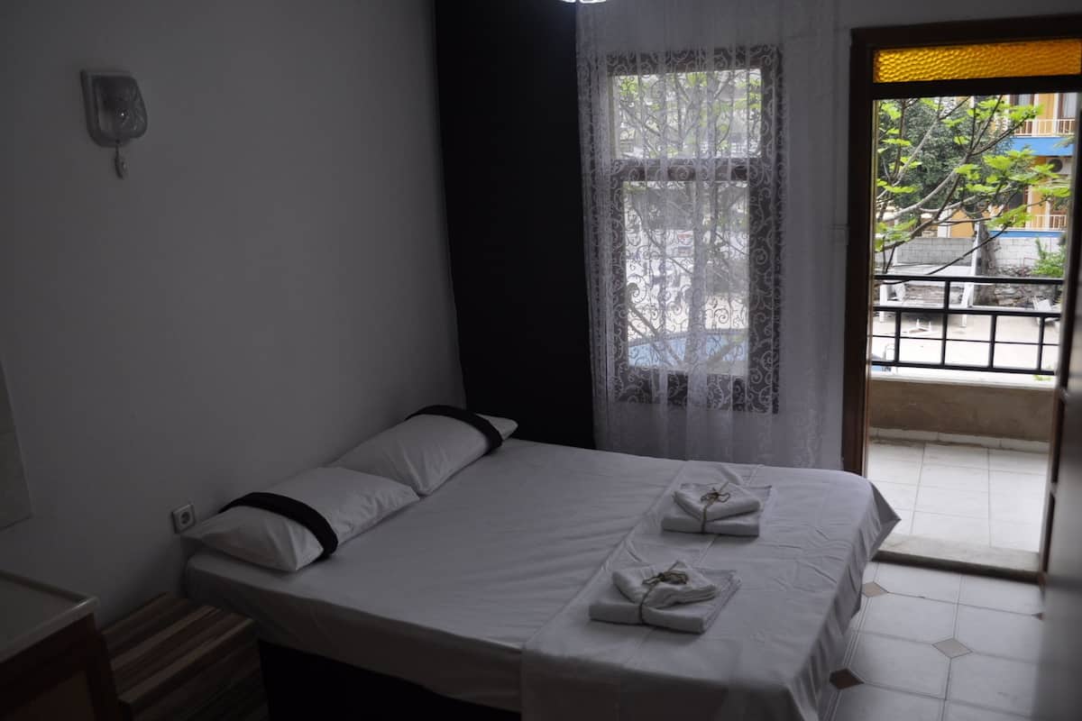 A hotel room with a bed, a window with a curtain, and a view of the outside.