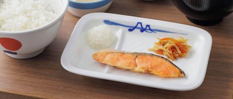 Variedad de platos japoneses, como arroz, pescado y verduras, servidos sobre una mesa de madera.