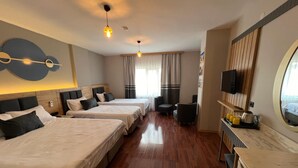 Habitación de hotel con tres camas, televisor, una pequeña zona de estar y mostrador de cocina.