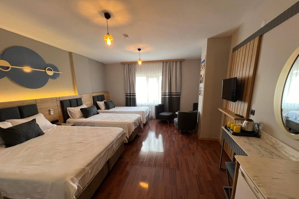 Quarto de hotel com três camas, televisão, um espaço de estar pequeno e bancada de cozinha.