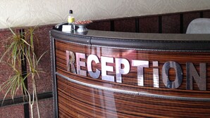 A reception desk with a wooden finish and the word "RECEPTION" in large letters. Above the desk, there is a wall with the text "MIDJAT GAP HOTEL" and three stars.