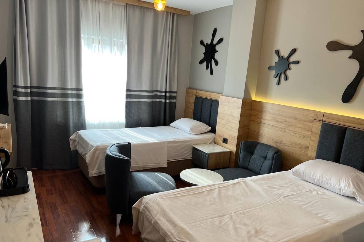 Quarto de hotel com duas camas, uma escrivaninha, uma cadeira e uma mesinha.