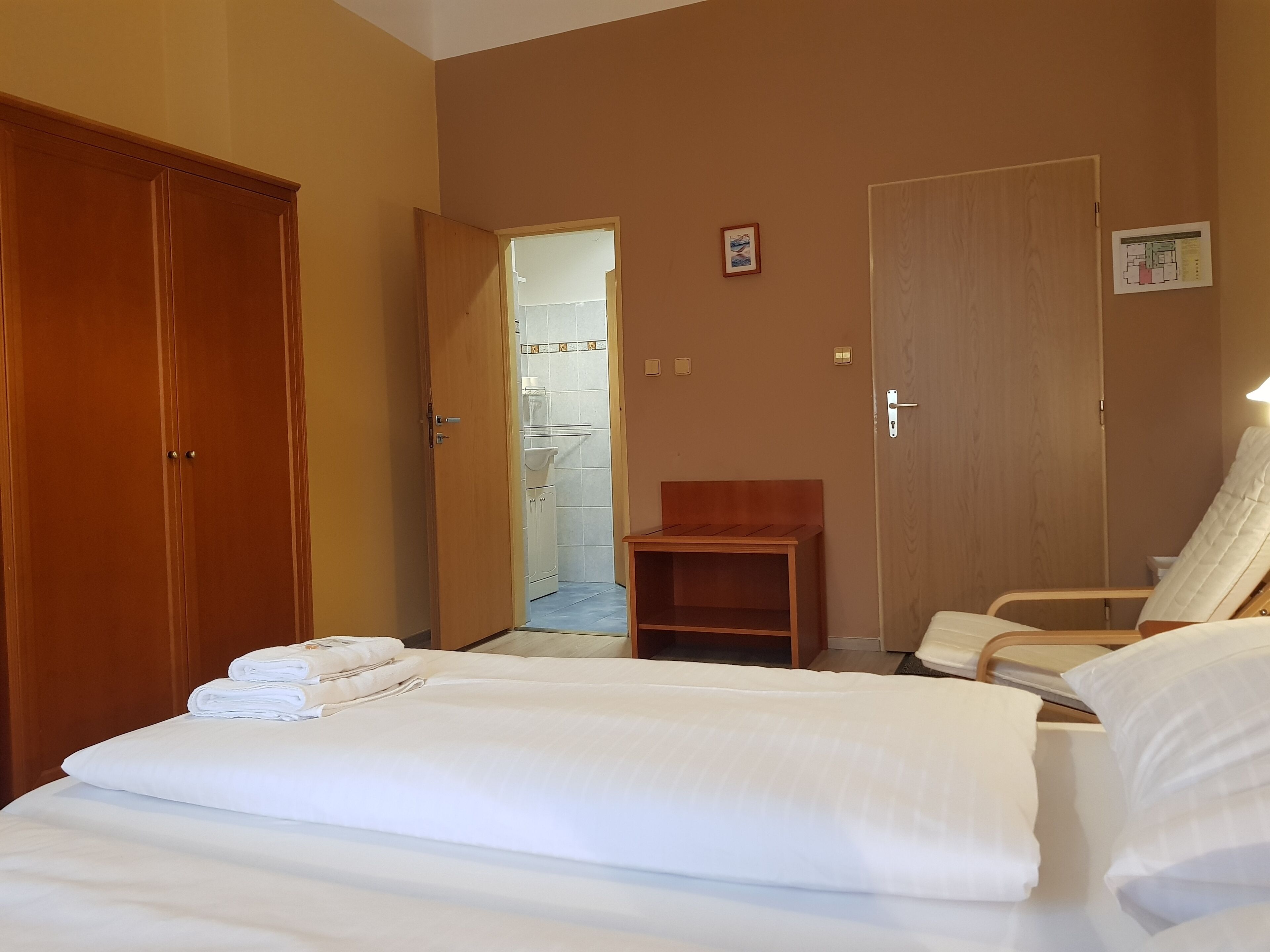 Une chambre d’hôtel avec un lit, une armoire en bois, une salle de bain visible à travers une porte ouverte et une chaise.