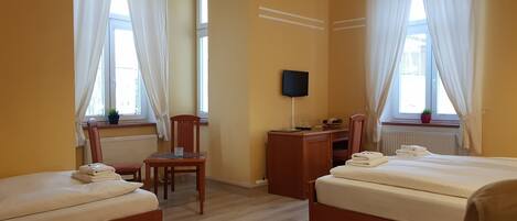 Habitación de hotel con dos camas, un escritorio, una silla, un televisor y ventanas con cortinas.