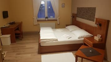 A hotel room with a wooden bed, a desk, a chair, a small table, and a radiator.