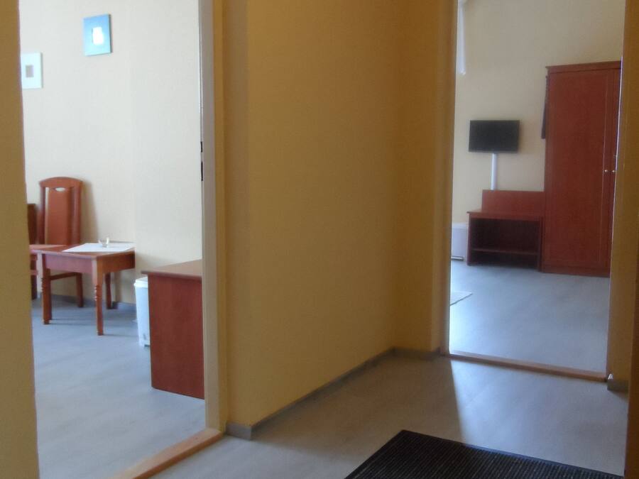 Un pasillo con piso alfombrado, una silla de madera, una mesita y un televisor sobre un mueble.