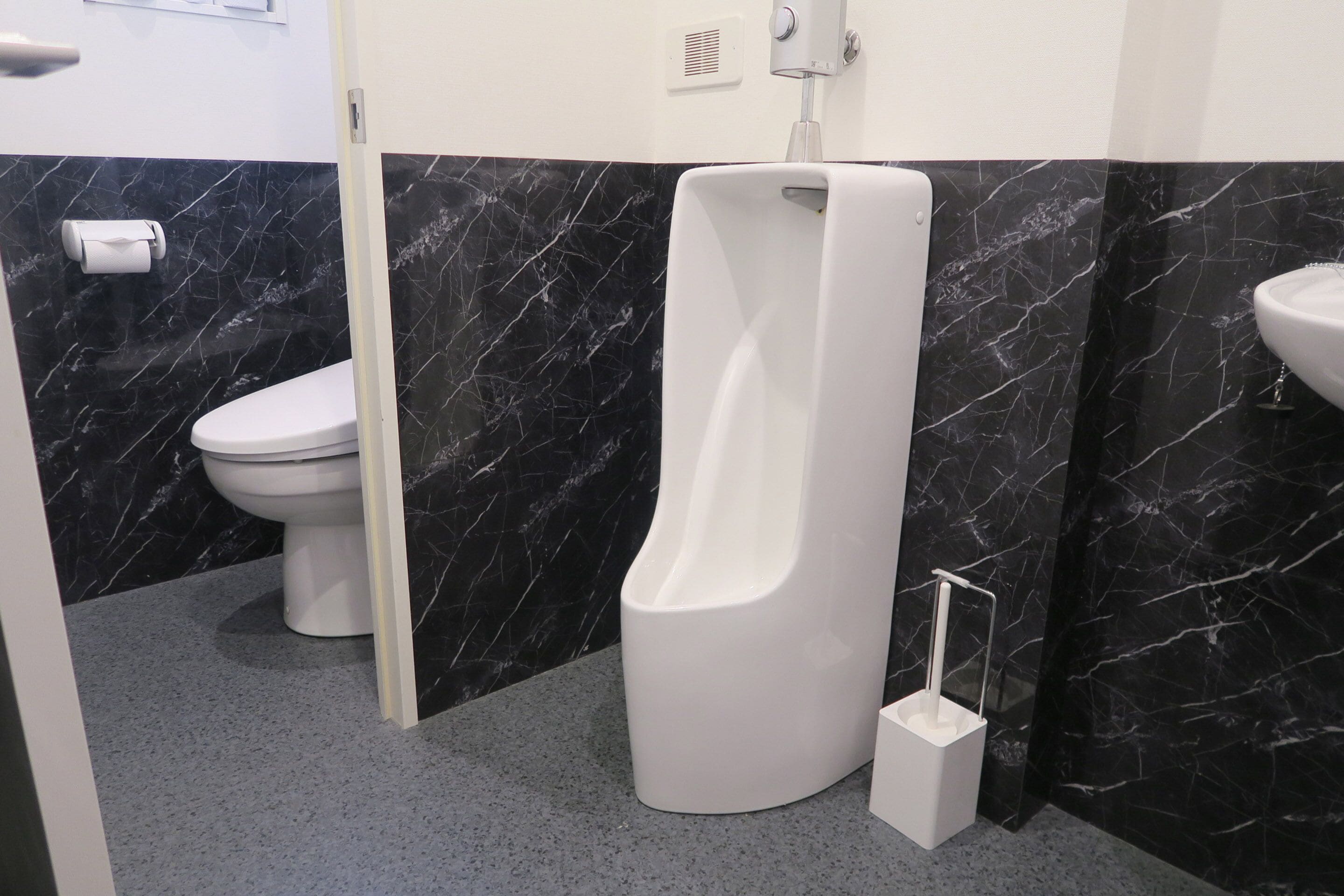 Un baño moderno con inodoro, orinal y lavamanos frente a paredes de mármol.