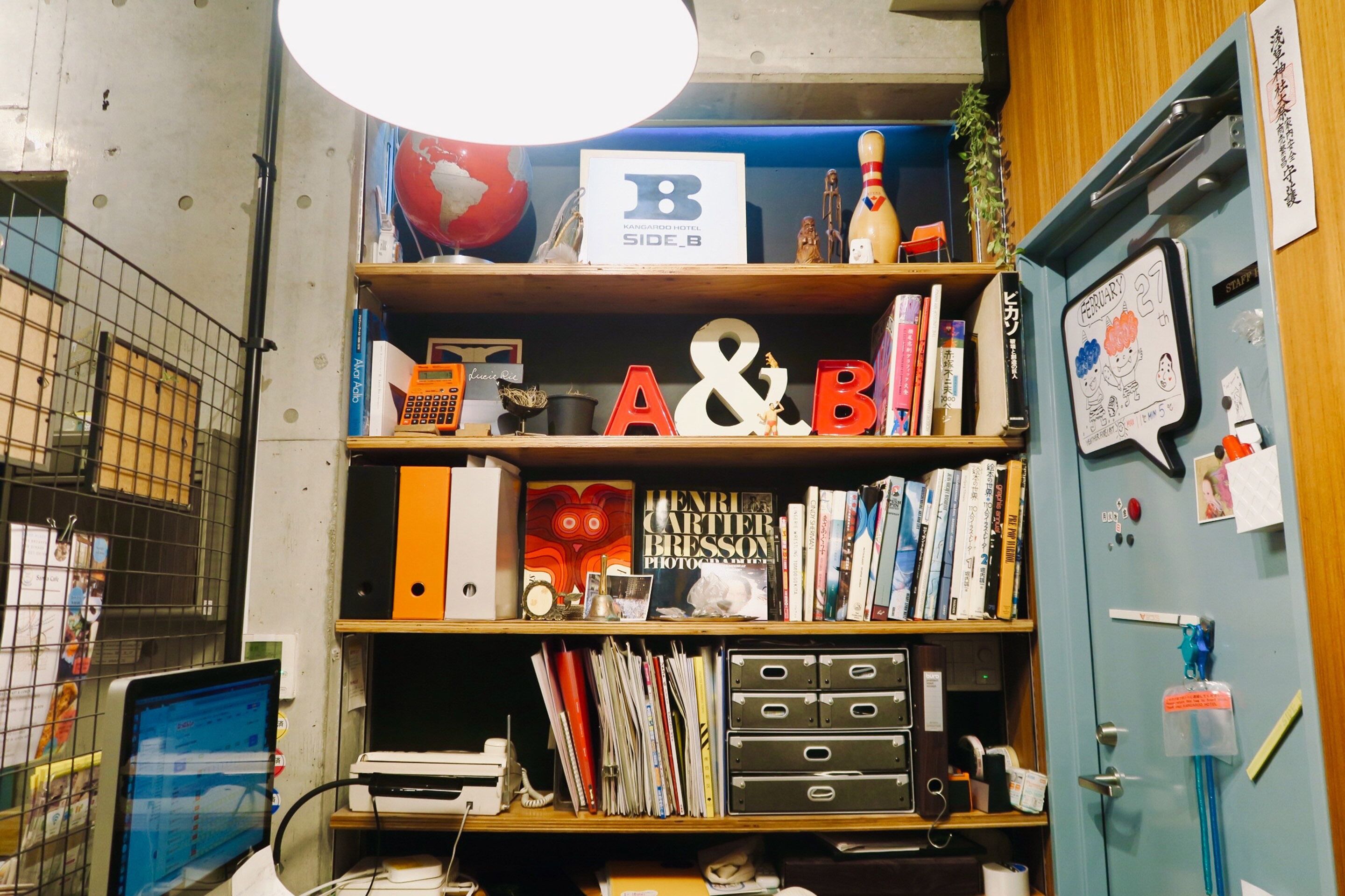 A room with a desk, shelves with books, a computer, and a blue cabinet with a calendar.