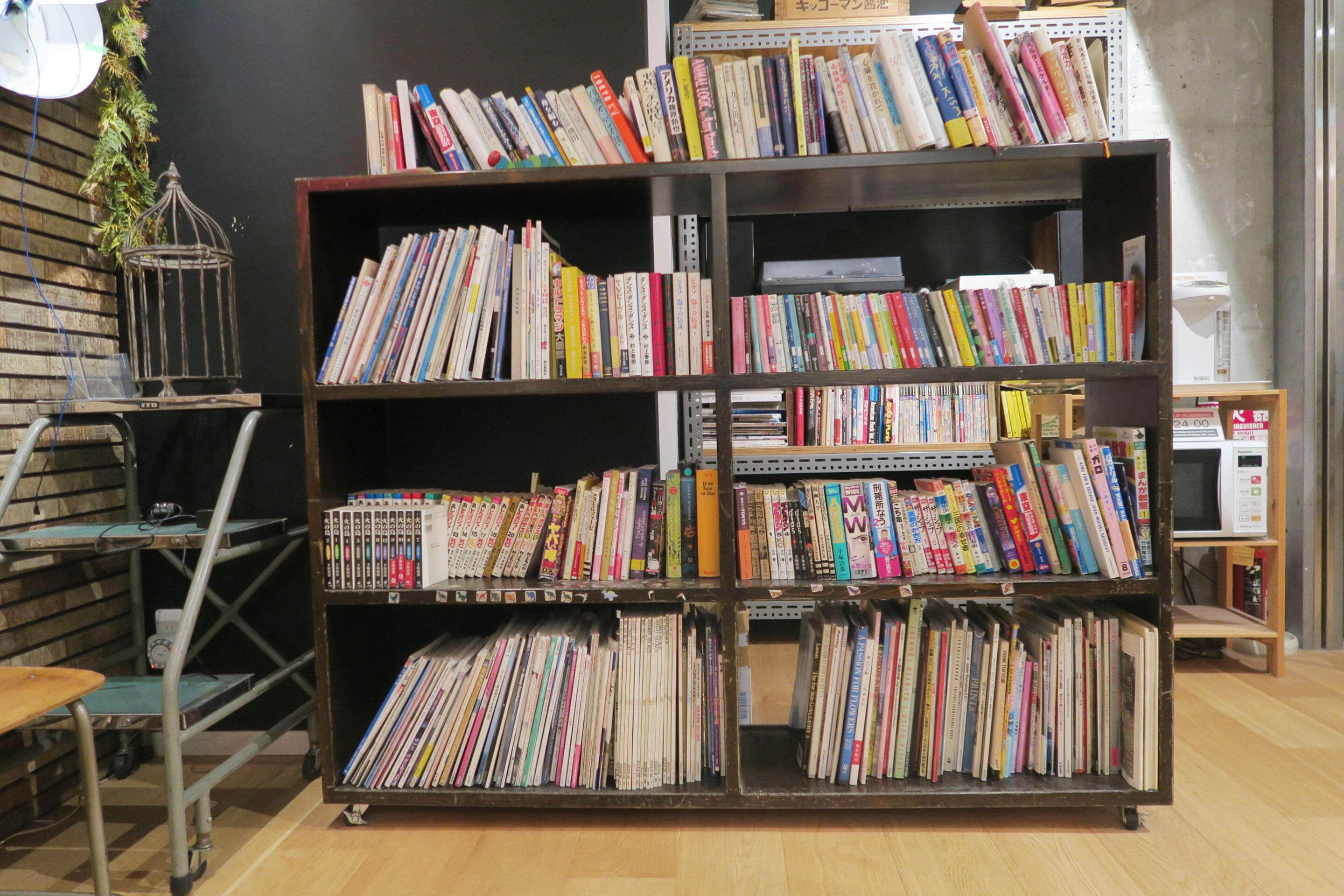 Una estantería llena de libros en una habitación con suelo de madera y un estante de metal.