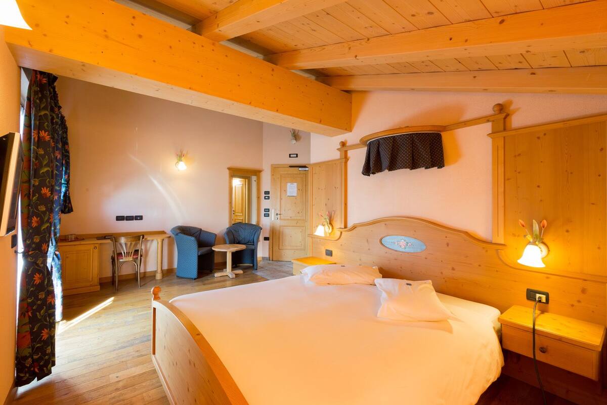 A cozy bedroom with a wooden bed, bedside tables, a desk with chairs, and a mirror.