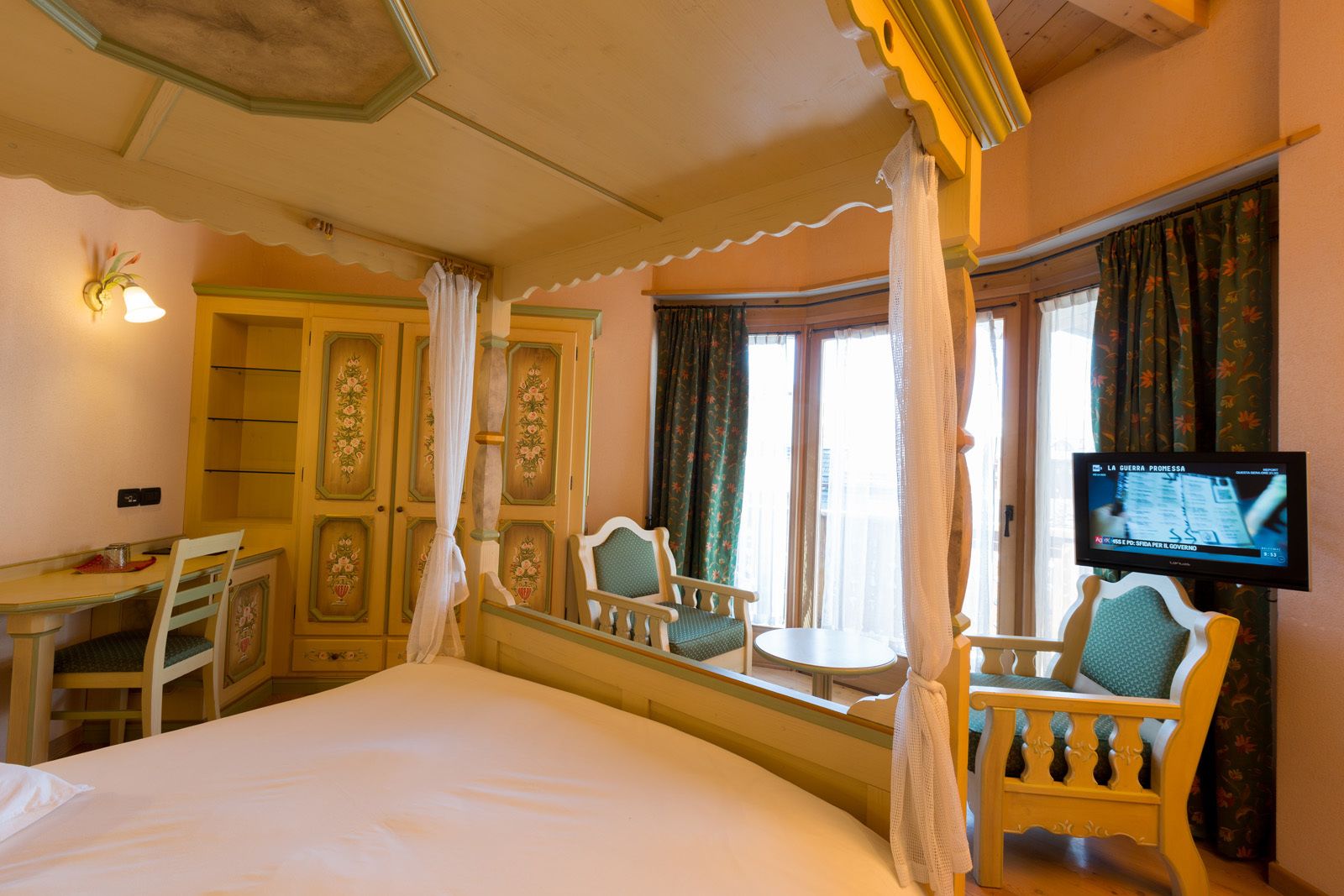 A hotel room with a bed, a desk, two chairs, a television, and a window with curtains.