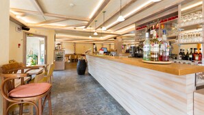 Un espace bar avec des meubles en bois, un comptoir orné de bouteilles et de verres, et un sol carrelé.