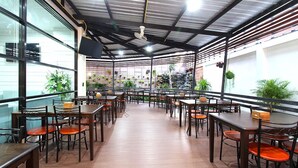 Un comedor interior con varias mesas y sillas, suelo de madera y techo con vigas metálicas y un ventilador.