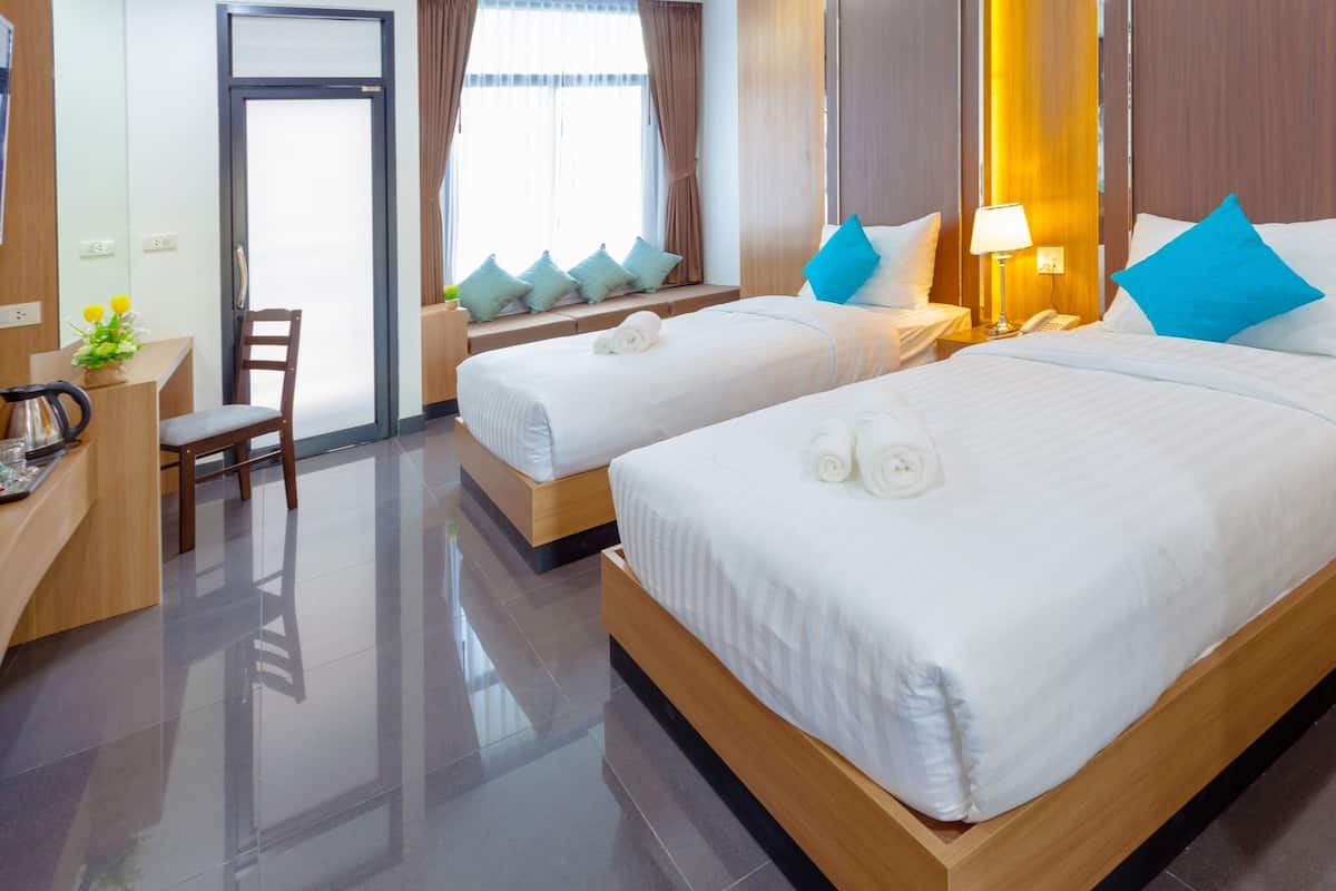 Ein Hotelzimmer mit zwei Betten, einem Schreibtisch mit Stuhl, einem kleinen Tisch mit Pflanze und einem Fenster mit Vorhängen.